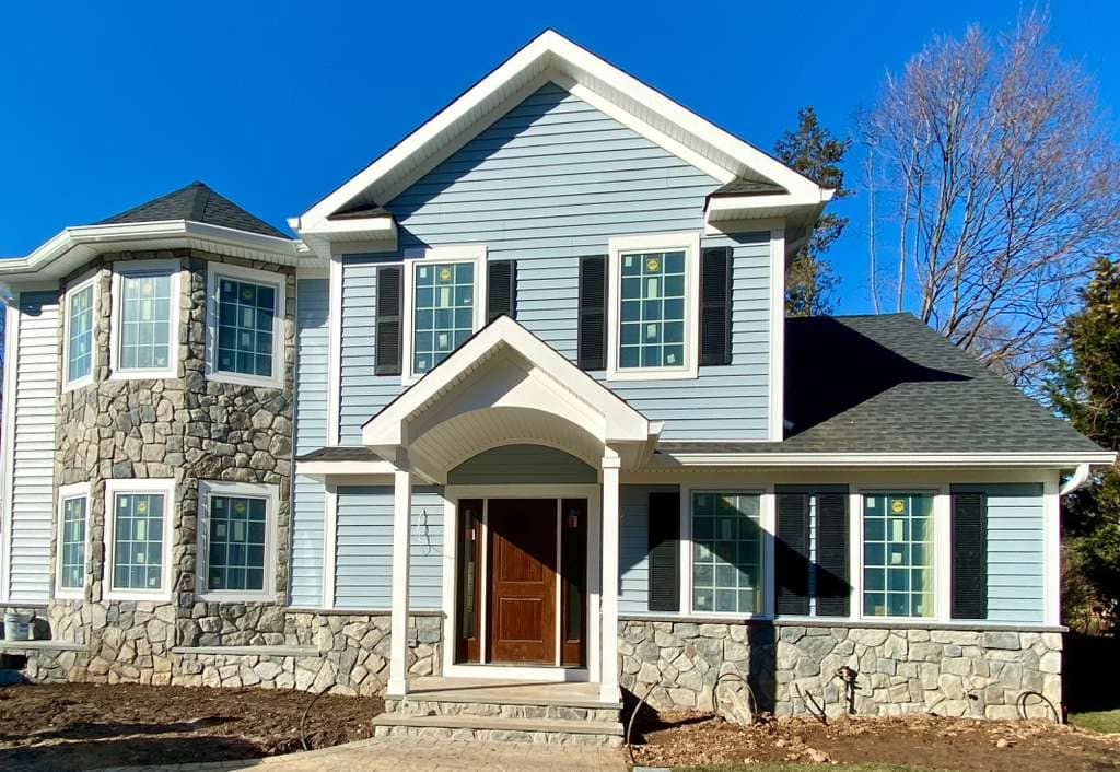 Front view of newly constructed two-story home with blue siding, stone veneer accents, and arched entryway installed by Legacy Contractor