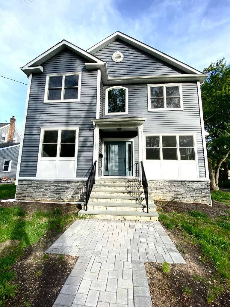 Newly renovated two-story residential home with gray siding, stone front steps, and modern entryway installed by Legacy Contractor NJ.
