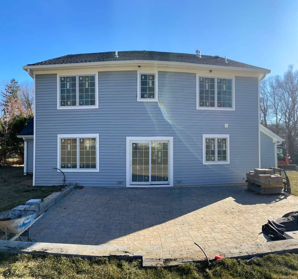 Side view of a newly renovated home exterior featuring dark blue horizontal siding, white trim, multiple windows, and exterior utility connections.